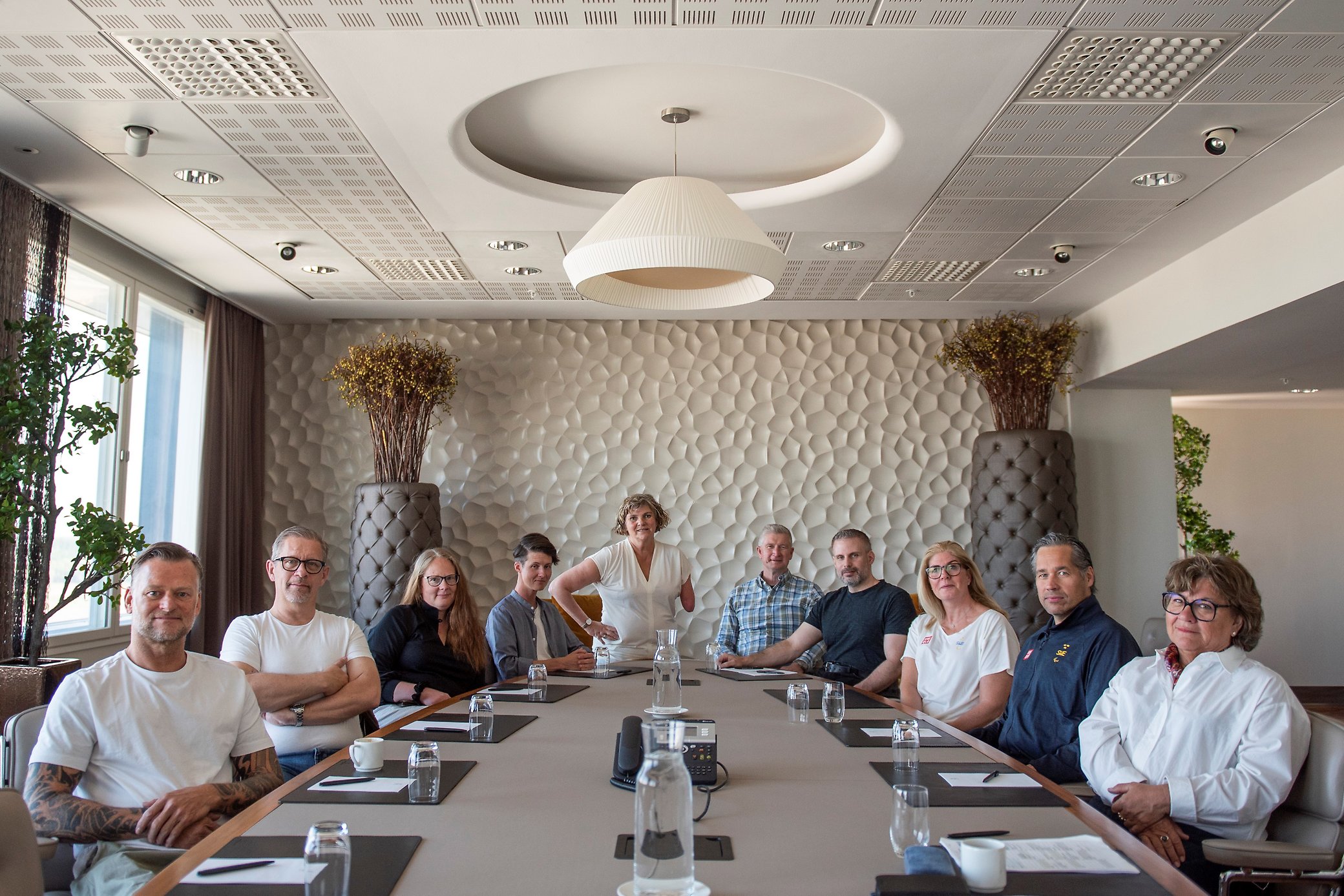 Bild på förbundsstyrelsen 2023-2025. Styrelsen sitter vid ett avlångt bord i ett konferensrum. I mitten står ordförande Åsa Llinares Norlin.