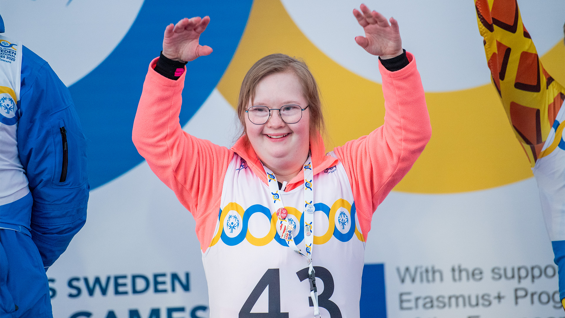En tjej med downs syndrom sträcker armarna i luften. Hon är med på en medaljceremoni för alpina skidåkare på Special Olympics Sweden Invitational Games i Östersund och Åre 2020.