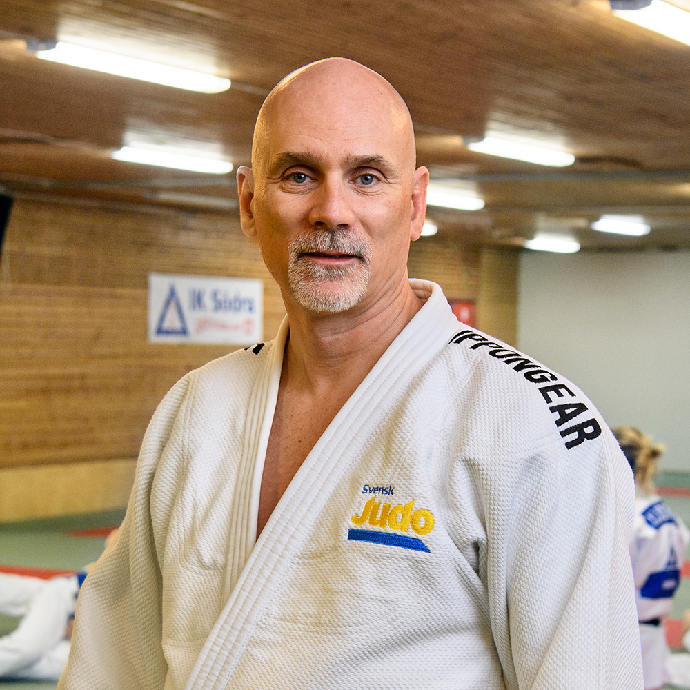 Porträttbild på Dick Rösselharth, ledare inom judo. Dick har på sig en judodräkt och står i en träningshall där judo utövas.